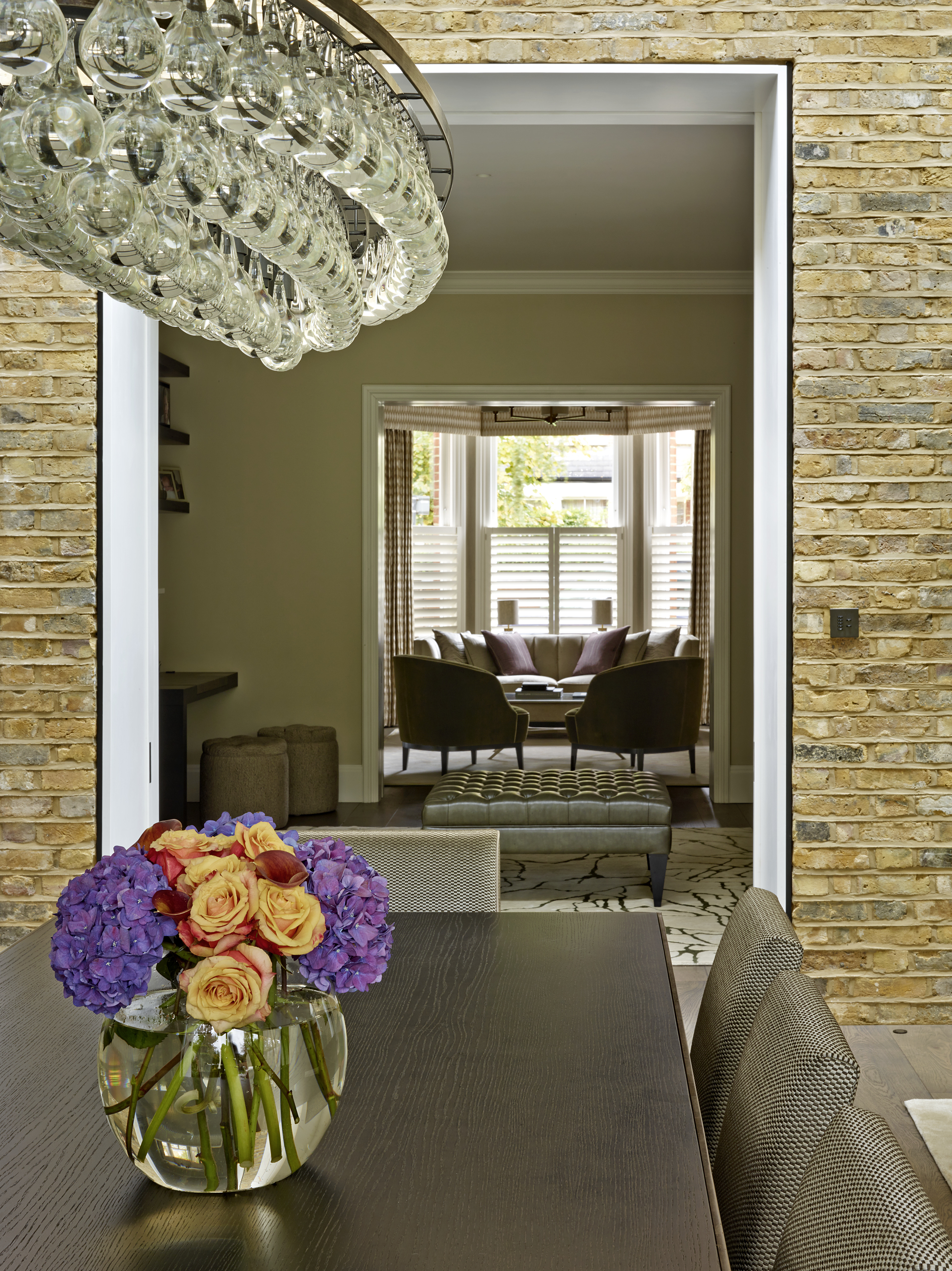 Oval shaped glass peardrop chandelier over dark oak dining table with bronze edges and satin upholstered dining chairs.