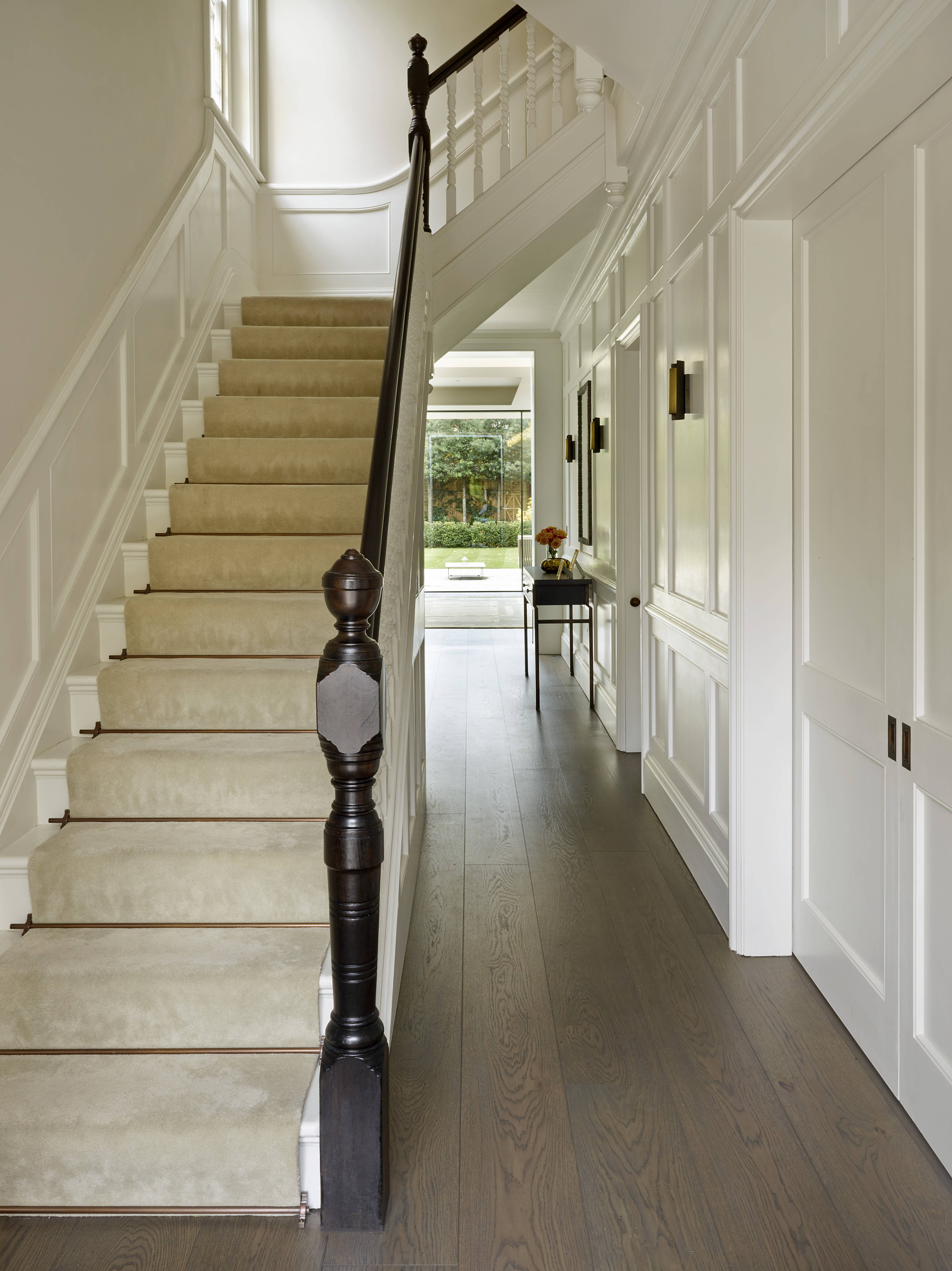 Smoked oak flooring in painted wood panelled hallway showing staircase with bronze stair rods and dark stained handrail.