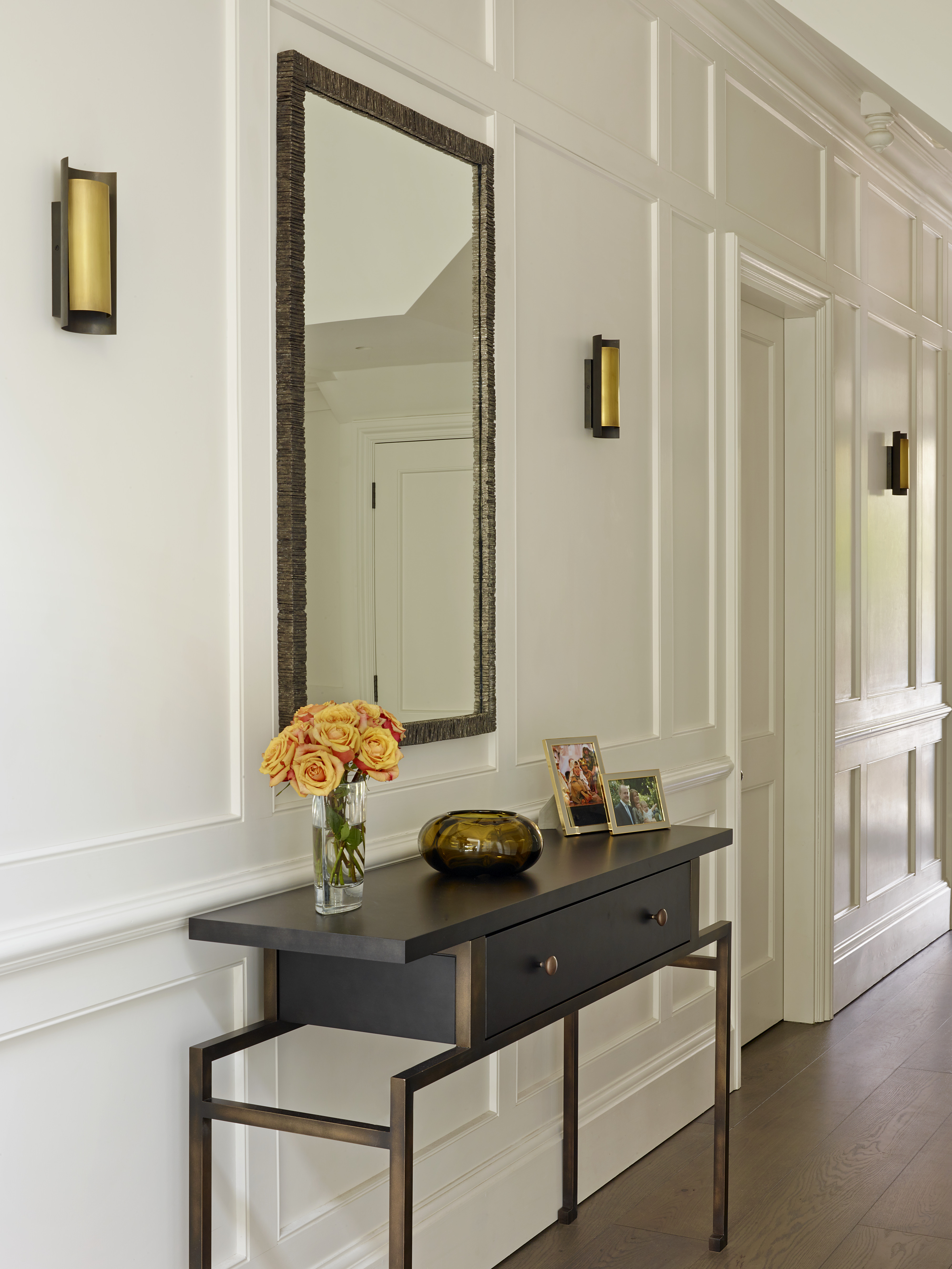 Painted wood panelled hallway with bronze & smoked oak console, brass and bronze wall lights and mirror.