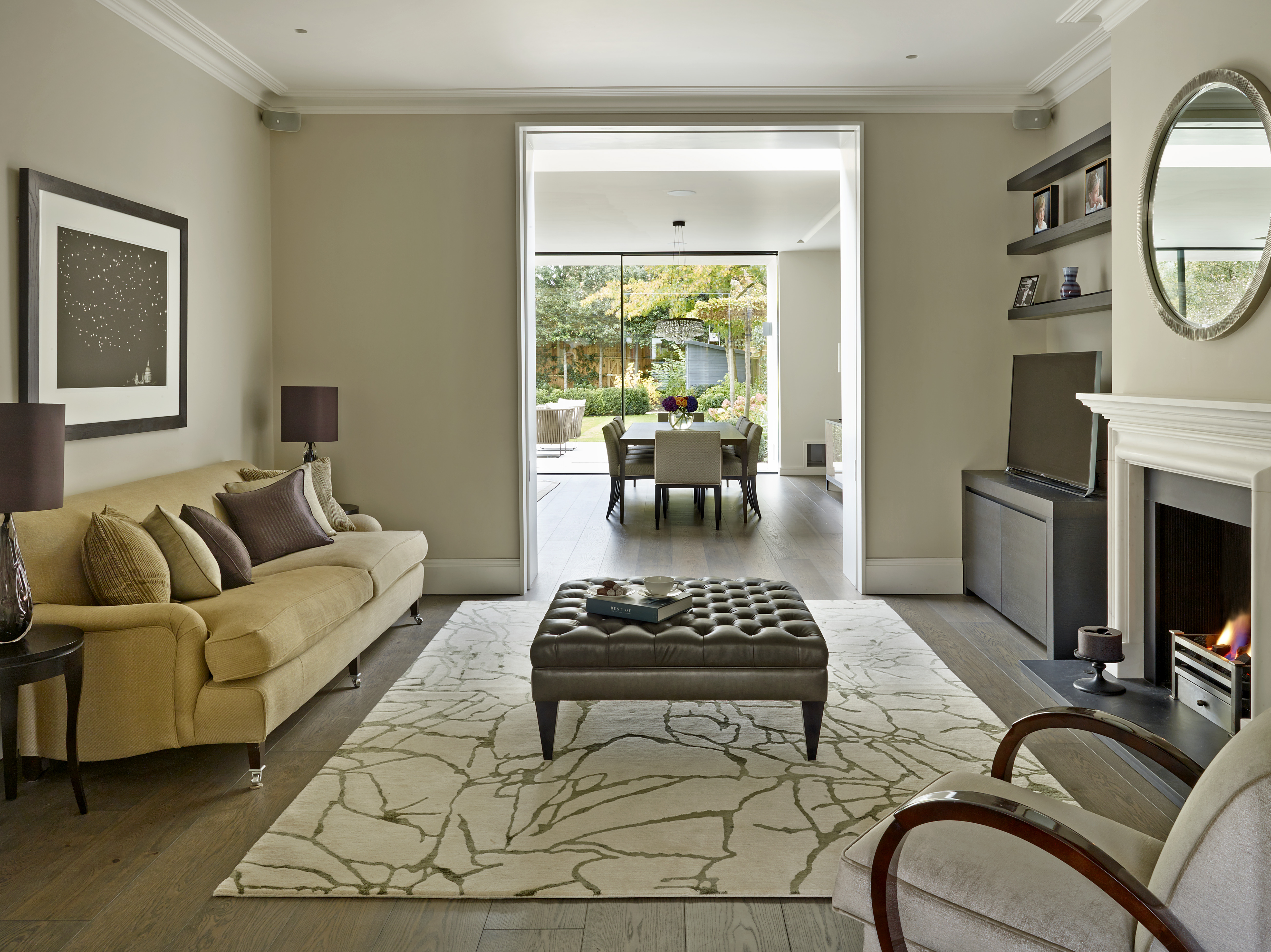 Relaxed family sitting room with wool and silk patterned rug and leather buttoned footstool leading through to dining area in kitchen extension.
