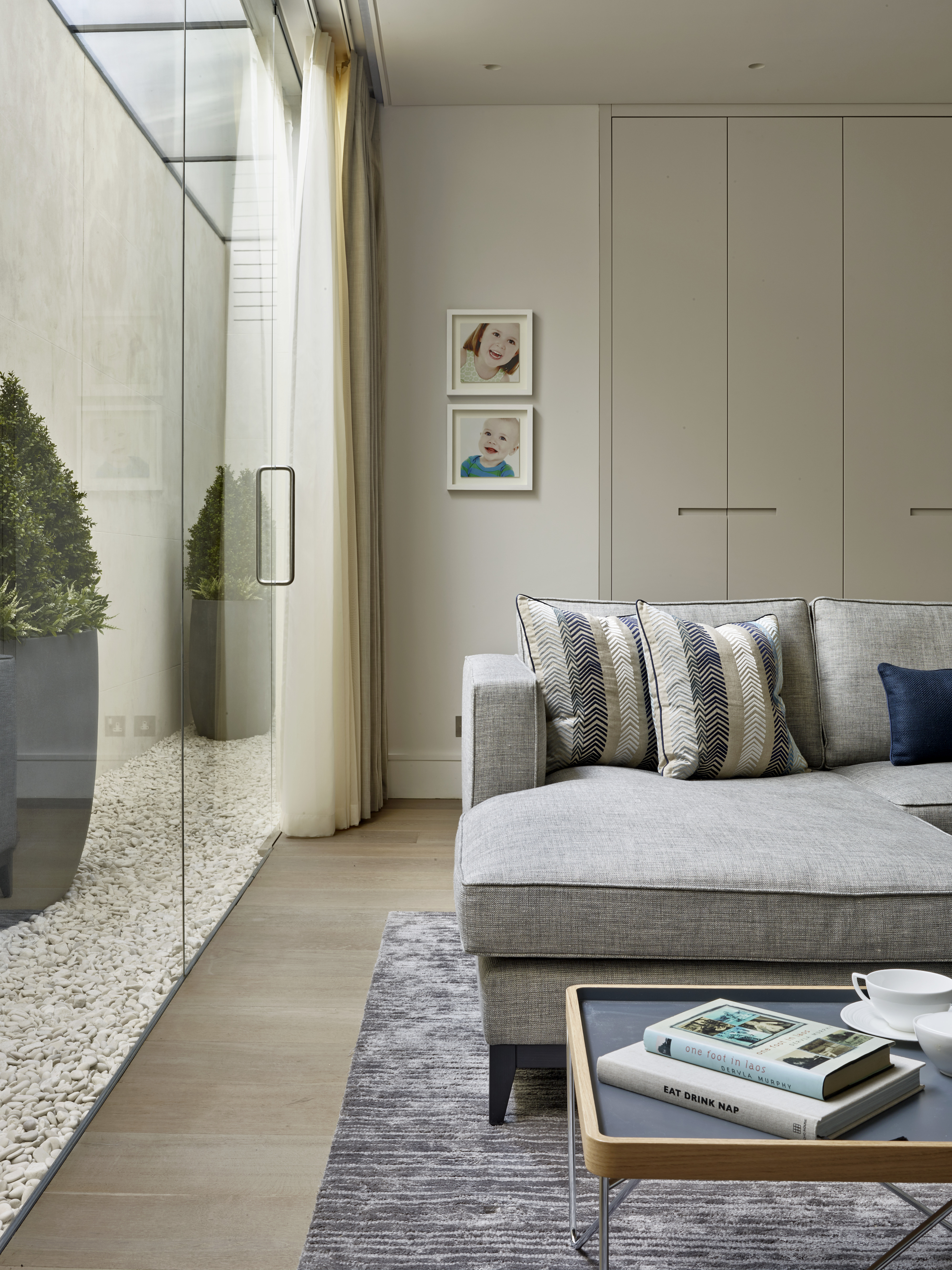 Contemporary styled sofa and cushions with matt lacquer storage cabinets beside glass wall leading to basement lightwell.