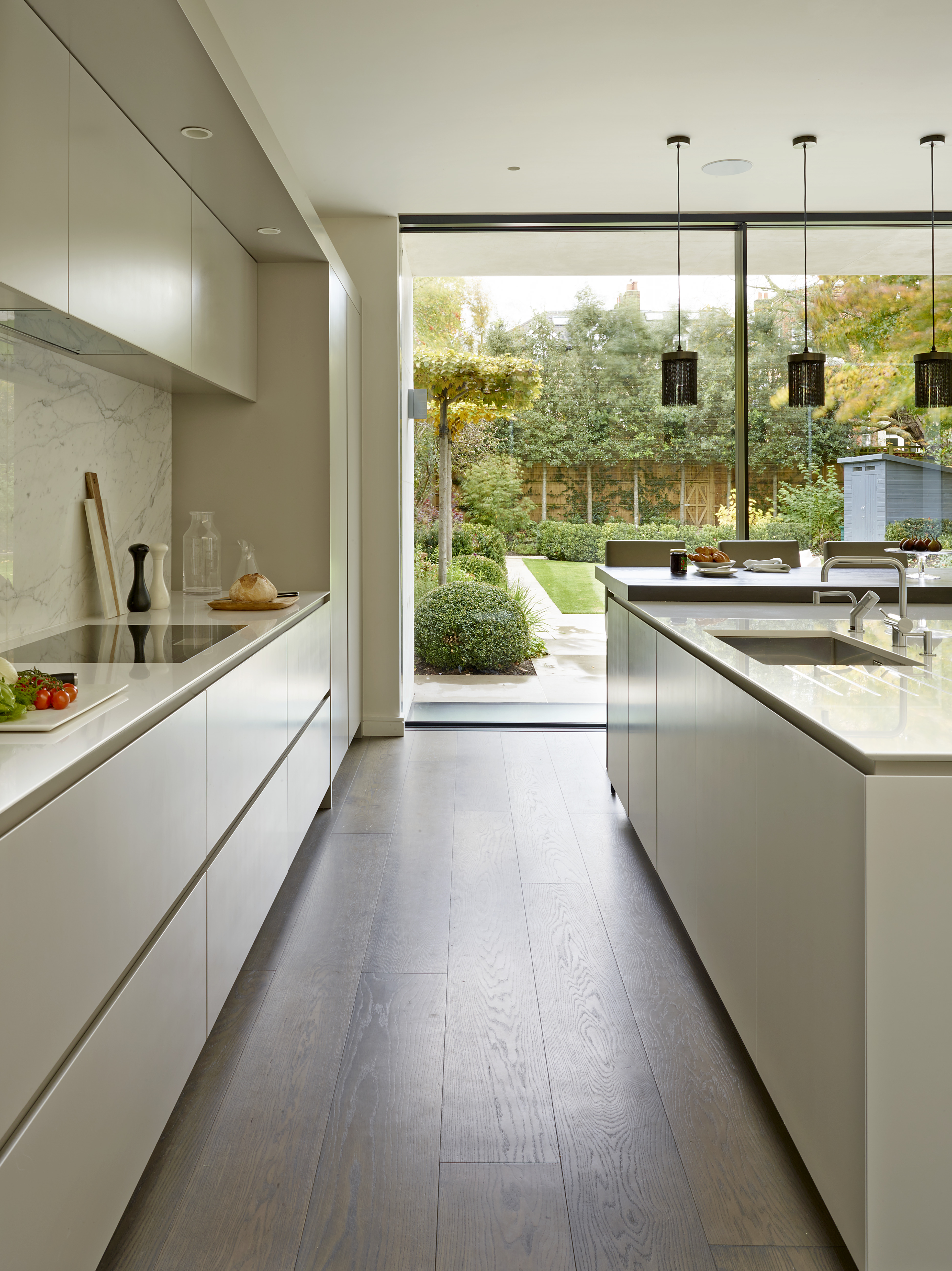 Contemporary kitchen scheme with composite stone worktops and bespoke lacquer cabinets bedside full length glass doors overlooking garden.